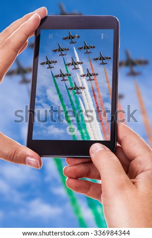 a woman using a smart phone to take a photo of an airshow performance