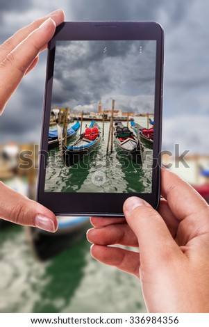 a woman using a smart phone to take a photo of some gondolas moored in Venice, Italy