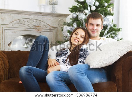 Young happy couple sitting on the sofa by Christmas tree
