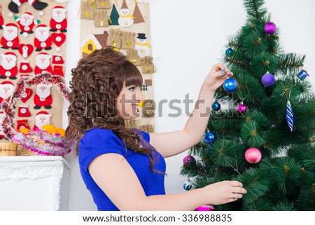 beautiful girl decorates her home before Christmas. beautiful girl decorates the Christmas tree. A woman in a beautiful dress and festive make-up preparing for the arrival of guests