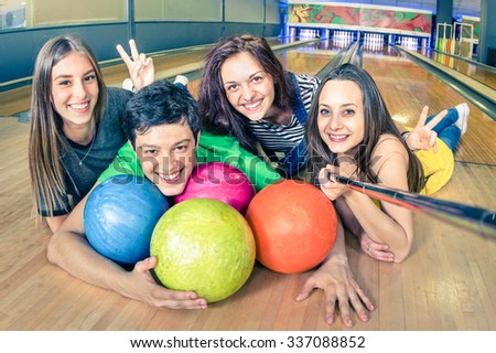 Best friends using selfie stick taking pic on bowling track - Friendship concept with young playful people having fun together - Soft focus on the guy with vintage filtered look and retro color tones