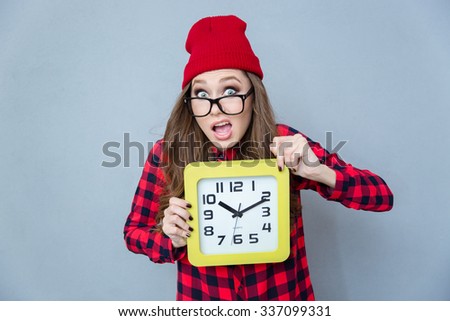 Portrait of a funny hipster woman holding wall clock over gray background