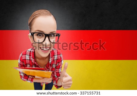 people, education, gesture and school concept - happy smiling teenage student girl with folders showing thumbs up over german flag background