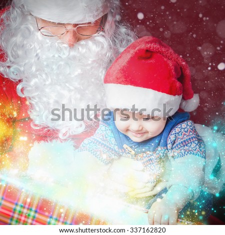 Christmas light and inspiration! Christmas baby wearing a Santa Claus hat and Santa opening a present and gift box! Night, xmas eve, surprise. Magical light. Design