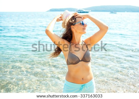 Beach vacation. Young woman in a hat and swimsuit walking on the beach on a hot summer day
