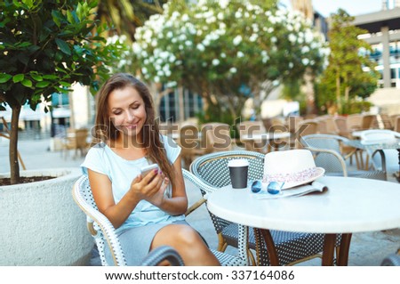 Young woman relaxing in the outdoor cafe - drinking coffee and using a smartphone