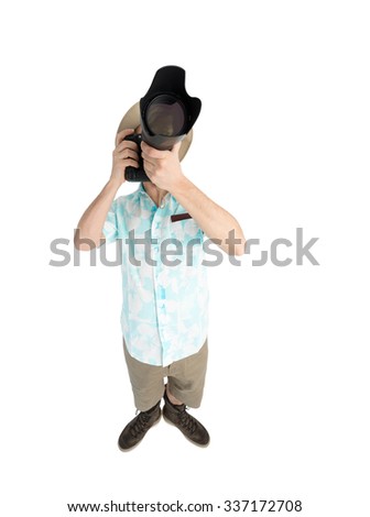Silly man tourist in blue shirt, brown shorts and hat holding big dslr camera and shooting. Traveler concentrating and making pictures. Isolated on white background.