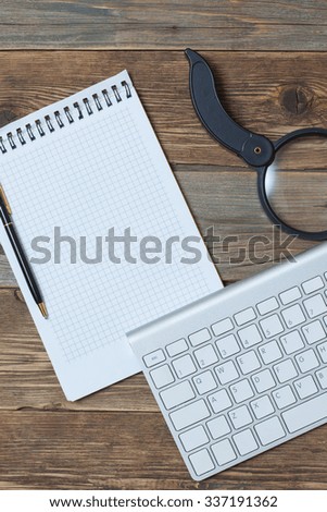 Computer keyboard, notebook, pen and magnifying glass on old wooden table surface. Still-life with objects for finding and recording information in the Internet space