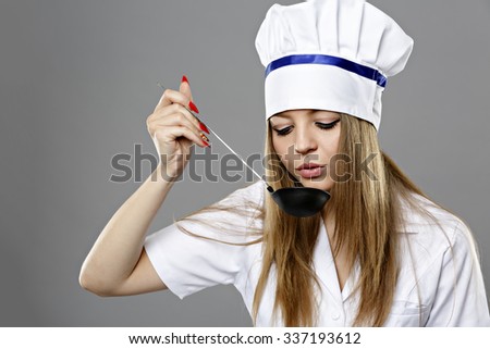 Woman chef holding a spoon and eating from spoon. On gray background.