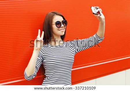Fashion pretty woman wear a sunglasses and striped dress makes self-portrait on smartphone over red background