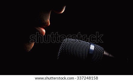 Part of a singer face, details of mouth and modern black microphone, on black background. 