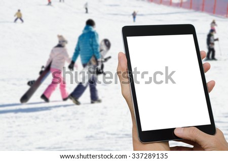 Hand holding tablet pc with isolated screen on white on blurred people at ski resort background .