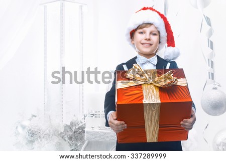 Beautiful little boy with a big Christmas gift in a Santa Claus hat. Christmas gifts for children. Smart boy Celebrates Christmas. New Year's holidays