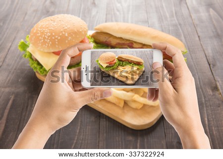 Friends using smartphones to take photos of hot dog and hamburger.