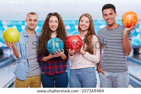 Young friends with bowling balls looking at camera