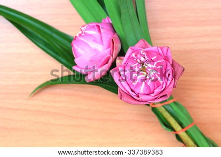 Bunch of pink lotus flowers bind with green pandan leaves on wooden background.