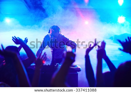 Energetic deejay standing in front of dancing people in club Royalty-Free Stock Photo #337411088