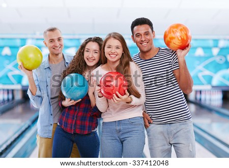 Group of joyful young friends with bowling balls looking at camera