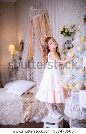 girl hangs Christmas decorations on the Christmas tree in her bedroom standing on a chair