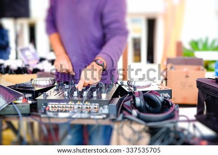 Picture of dj mixing audio tracks with professional musical equipment. Closeup of male hands and equalizer on blurred outdoor background.