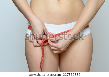 Young blond woman measuring her hip against grey wall Background