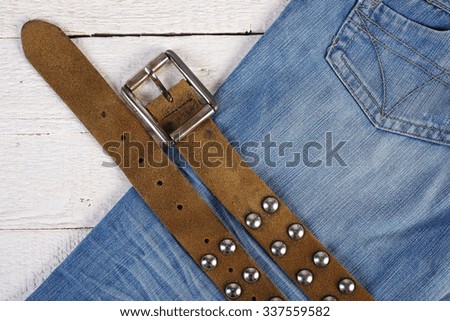 Man's concept set - Leather belt with metal rivets and blue jeans on a wooden background.