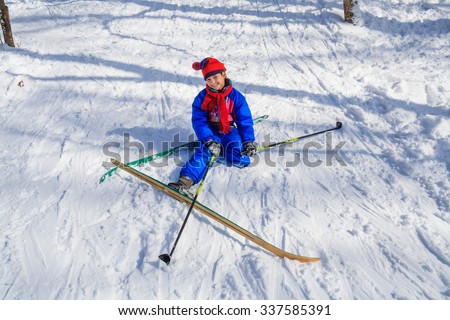 Happy girl sitting down on the snow learning skiing in the forest
