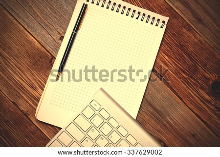 Computer keyboard, notebook and pen on the textured surface of an old wooden table. instagram image filter retro style