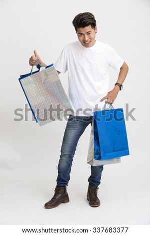 Cheerful smart young man showing thumbs up with shopping bags.
