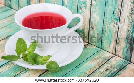 A cup of hibiscus tea with fresh mint leaves over wooden background