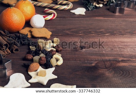 On a wooden desk background Christmas composition - candy cane, dough figurines, Christmas-tree branch Christmas balls, raisins, nuts, cinnamon sticks, cookies, star anise, mandarins; bump