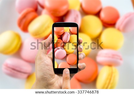 hand with smartphone photographing a plate of macarons  Royalty-Free Stock Photo #337746878