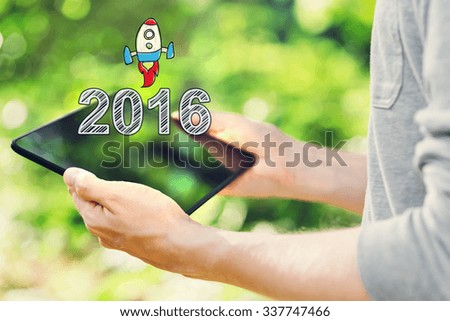 2016 concept with young man holding his tablet computer outside in the park  