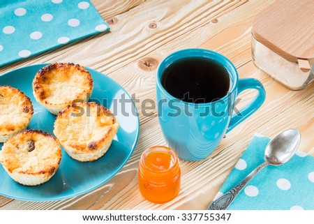 ruddy cheesecakes on blue plate, black tea in blue cup, blue napkin at white polka dots,  apricot jam in jar, sugar-bowl on wooden table
