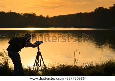 Silhouette of a nature photographer framing a shot, taking pictures by a lake at sunset