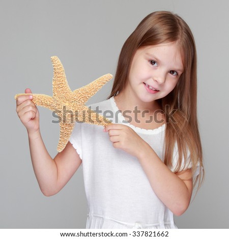 Positive little girl with a charming smile holds a large sea star on a gray background