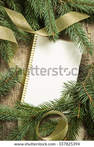 Christmas tree branches with blank sheet of notebook and golden ribbon on wooden background. Top view image of christmas decoration