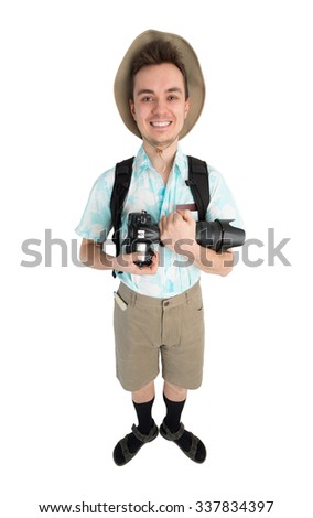 Happy man tourist in blue shirt, brown shorts and hat with backpack on his shoulders holding dslr camera. Traveler smiling and going to photo tour. Isolated on white background.