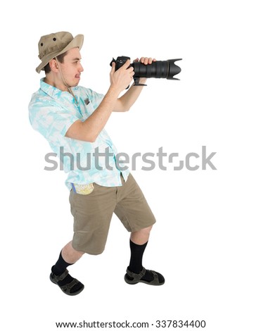Silly man tourist in blue shirt, brown shorts and hat holding big dslr camera and shooting. Traveler concentrating and making pictures. Isolated on white background.