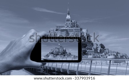 Female hand with smartphone taking a picture of Mont Saint Michel, France. Tourism concept.