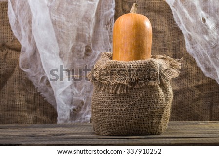 Photo closeup autumn still life one big whole fresh orange pumpkin gourd in sackcloth bagging standing on wooden table over rustic background, horizontal picture 