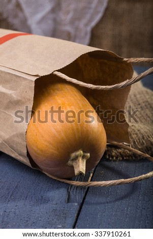 Photo closeup autumn still life one big whole fresh orange pumpkin gourd lying in paper packet near sackcloth coarse fabric on blue wooden table over rustic background, vertical picture 