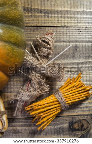 Photo top view sheaf of delicious straws tied together with string one side of big fresh orange pumpkin and voodoo doll with sticks on chest on wooden table on timber background, vertical picture 