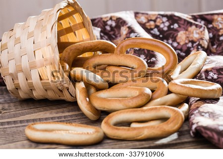 Photo still life closeup basket lying sidelong with delicious hard oval cracknels poured out on wooden table near flowery cloth over sunny rustic background, horizontal picture 