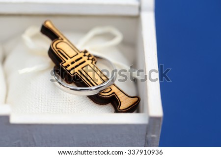 Closeup view of small wooden musical instrument of saxophone lying in white box with silver ring on blue background, horizontal picture