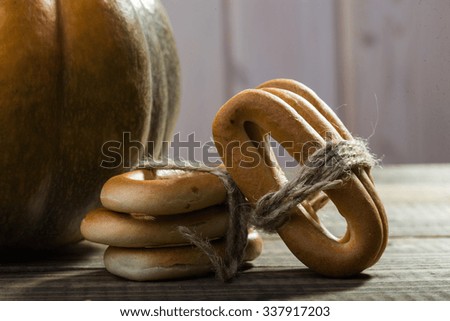 Photo closeup rustic autumn still life partial fresh orange pumpkin with bunches of hard oval cracknels bind with string on wooden table on timber background, horizontal picture 