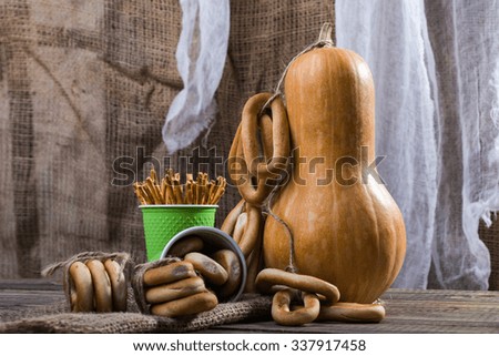 Still life big gourd with bunches bind with string lying on sackcloth two disposable green cups with straws and hard oval cracknels standing on wooden table on rustic background, horizontal picture 