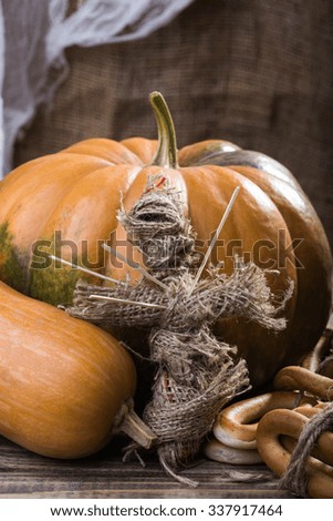 Photo still life bunches of hard oval cracknels bind with string orange gourd pumpkin and voodoo doll with sticks on chest on wooden table on blurred rustic background, vertical picture 