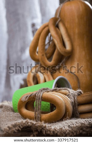 Still life closeup one big gourd standing with bunches of hard oval cracknels bind with string lying on sackcloth peeking out of disposable green cup on blurred rustic background, vertical picture 