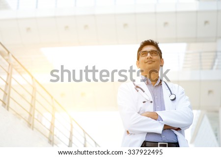 Portrait of confident Asian Indian medical doctor standing outside hospital building, beautiful golden sunlight at background.